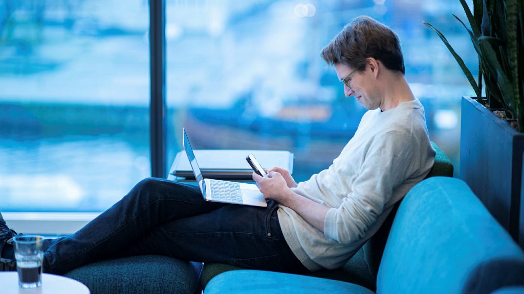 Man med dator i knät använder mobiltelefon på Internetstiftelsens kontor.