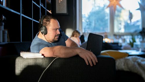 Man med hörlurar sitter i soffa i vardagsmiljö och använder dator.
