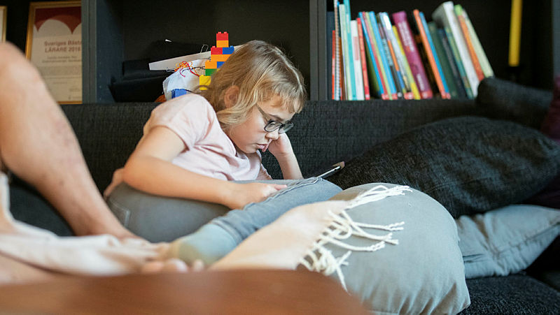Ett barn sitter i en soffa och tittar ner på en padda.