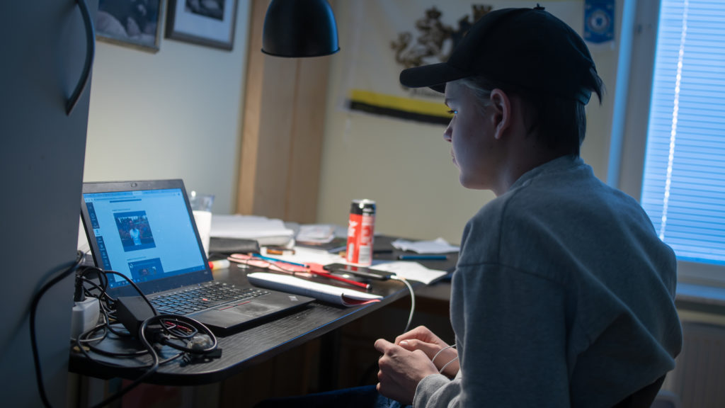 En kille med keps sitter framför sin dator vid ett skrivbord i sitt rum hemma och studerar