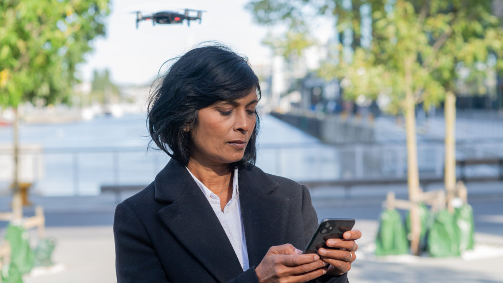 Kvinna använder mobiltelefon och övervakas av en flygande drönare.