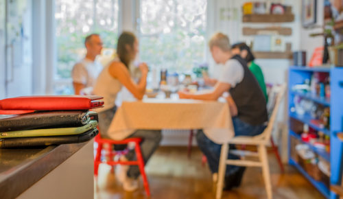 Familj med två tonårsbarn sitter och samtalar vid ett köksbord medan mobilerna ligger i en hög på diskbänken