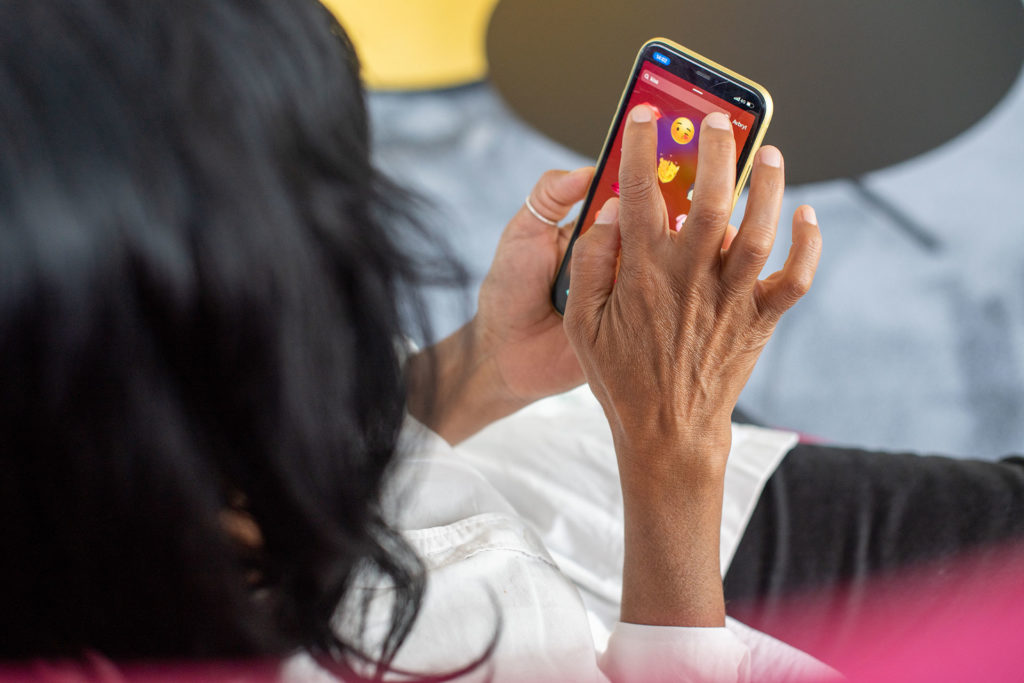 En kvinna trycker på sin smartphone, i skärmen syns emojis. 