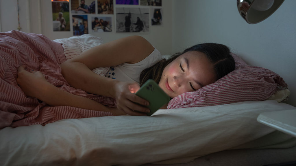 En ung tjej ligger och surfar på mobilen innan hon ska sova.
