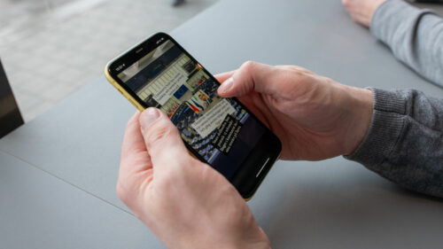 Händer som håller i en smartphone, på skärmen syns en bild från riksdagen.