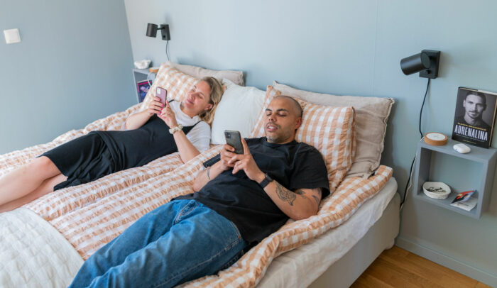 Man och kvinna ligger i sängen och surfar på varsin mobil.