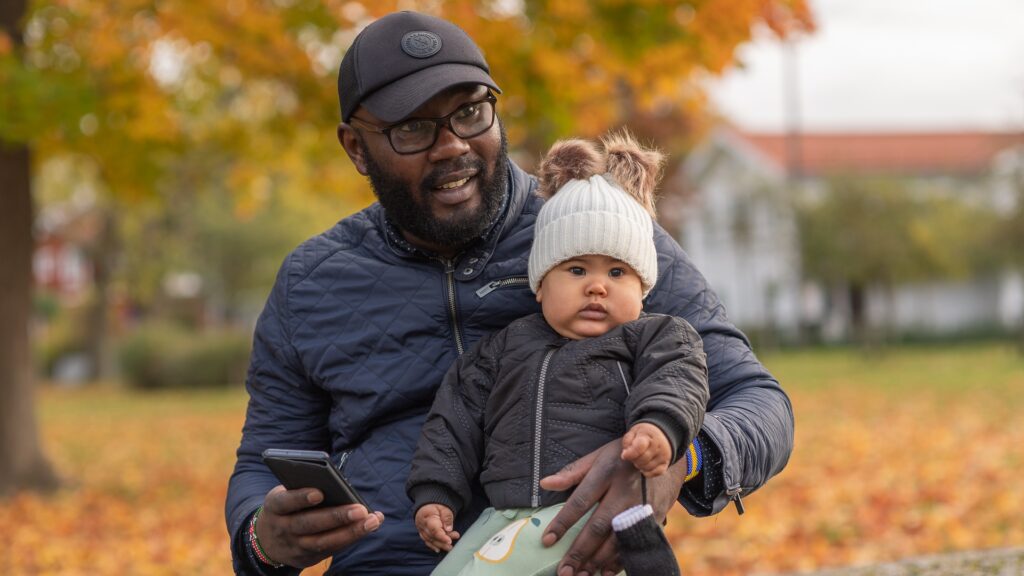 Pappa utomhus med sitt barn och en mobiltelefon.