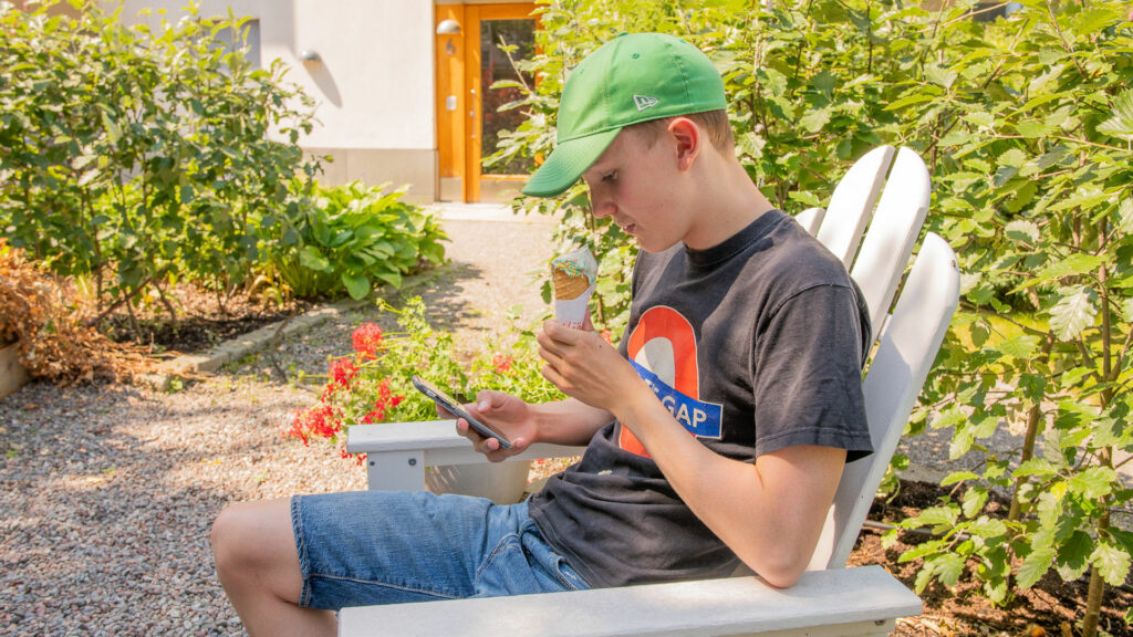 Ung kille äter glass och surfar på sin mobil.