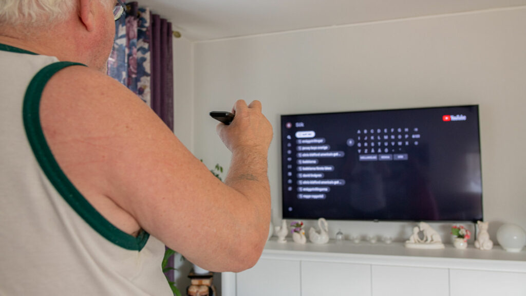 Äldre man söker med fjärrkontroll på en smart-tv.