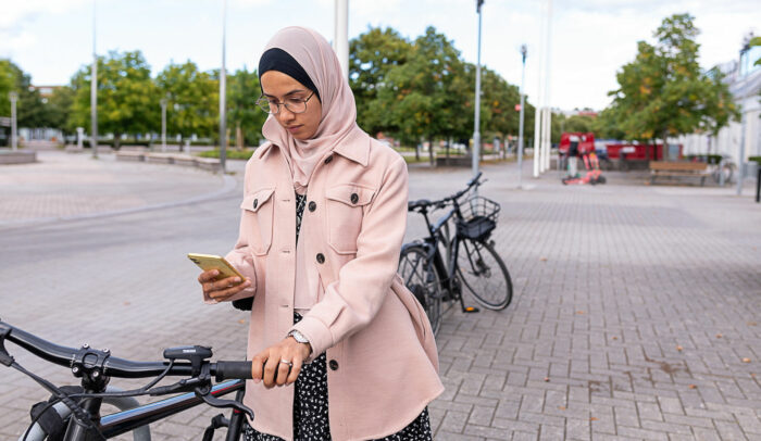 Kvinna leder en cykel och kollar på sin mobil.