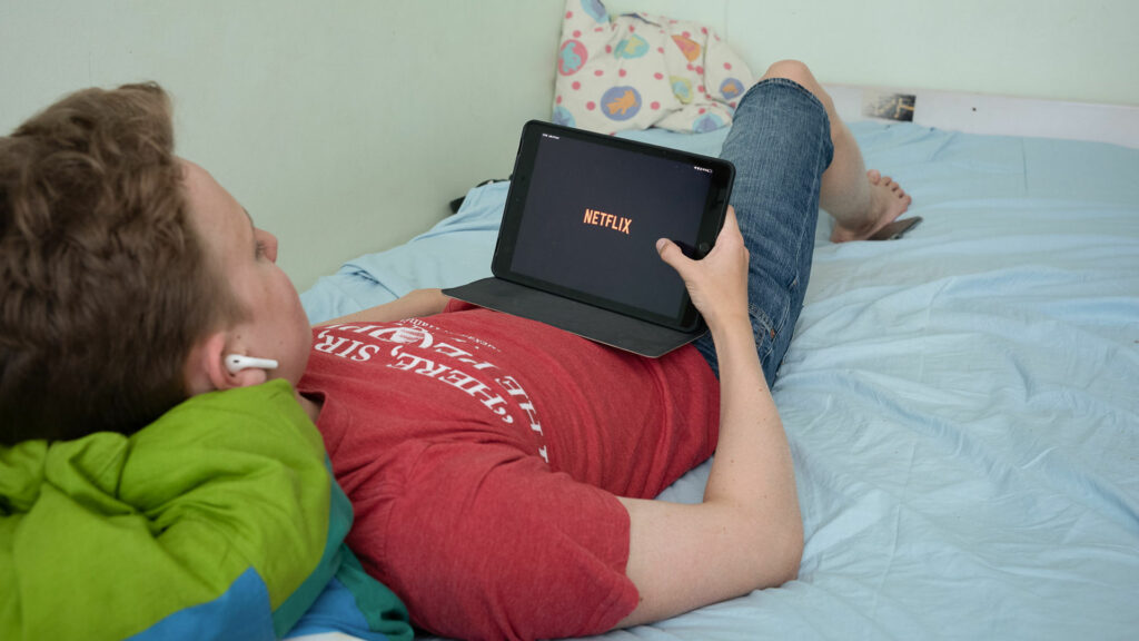 Ung kille ligger i soffan och kollar på Netflix på en surfplatta.