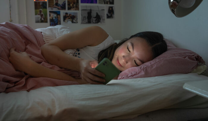 Tjej född på 2000-talet ligger i sängen och tittar på sin mobil.