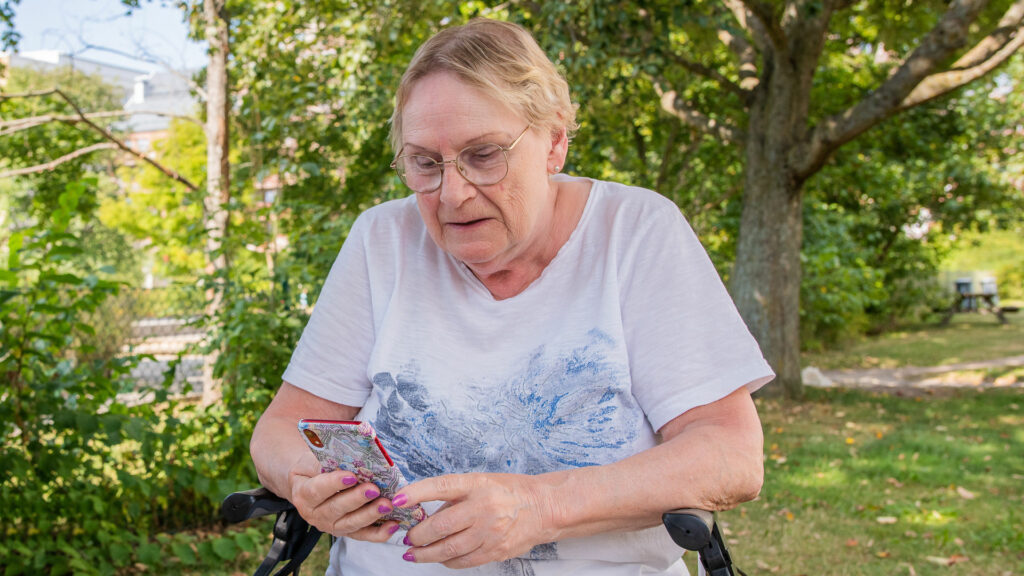 Äldre kvinna med rullator tittar oroligt på sin mobiltelefon.