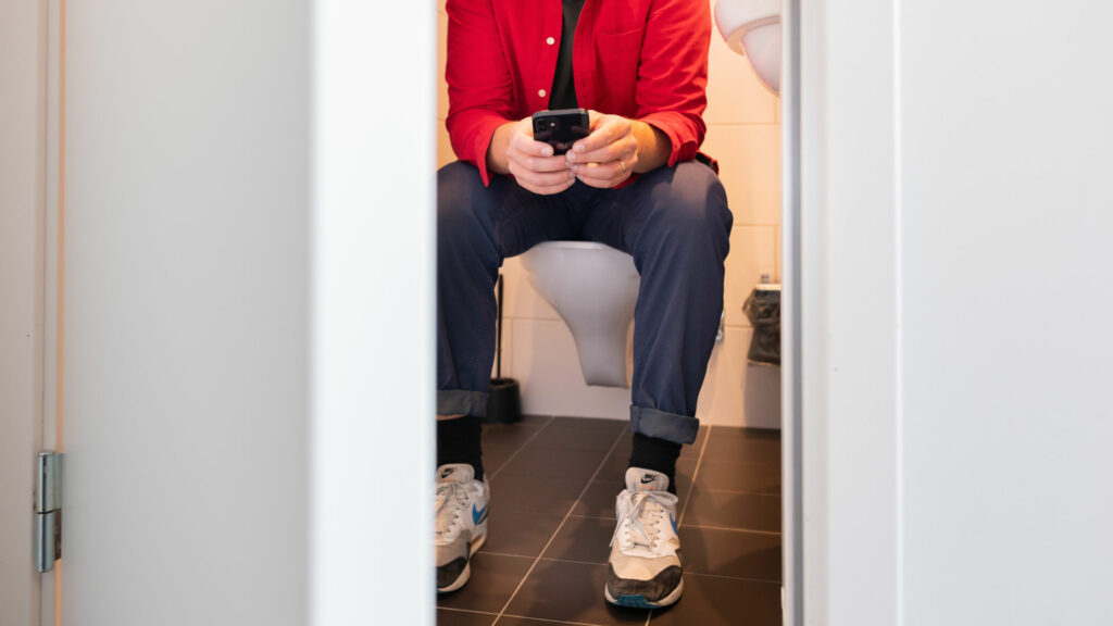 Man sitter inne i badrummet och surfar på sin mobil.