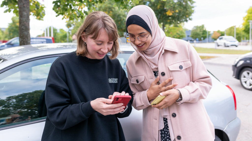 Två kvinnor tittar på en mobiltelefon utomhus.