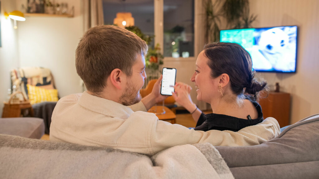 Man och kvinna sitter i en soffa tillsammans och kollar på en mobil.