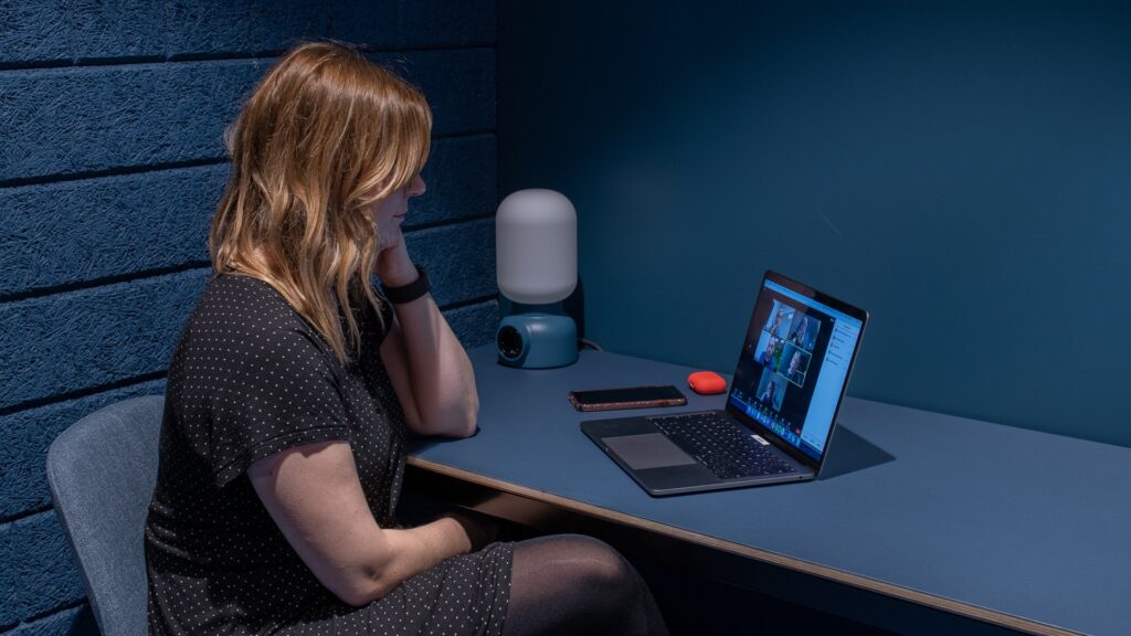 En kvinna sitter i ett mörkt rum och har ett digitalt möte. Hållbarhet.