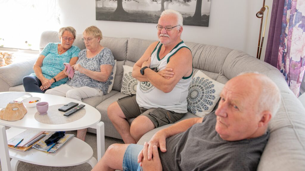 Fyra äldre personer sitter i en soffa, två av dem tittar tillsammans på en mobil.