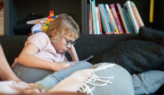 Ett barn sitter i en soffa och läser e-bok på en surfplatta.