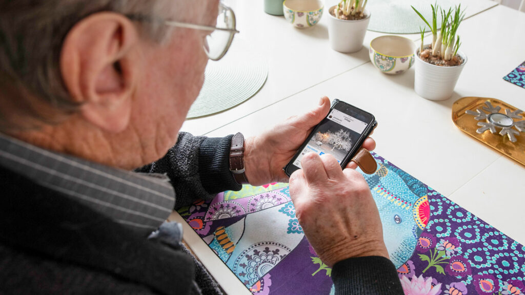 En äldre man sitter med mobilen och delar något på Instagram.