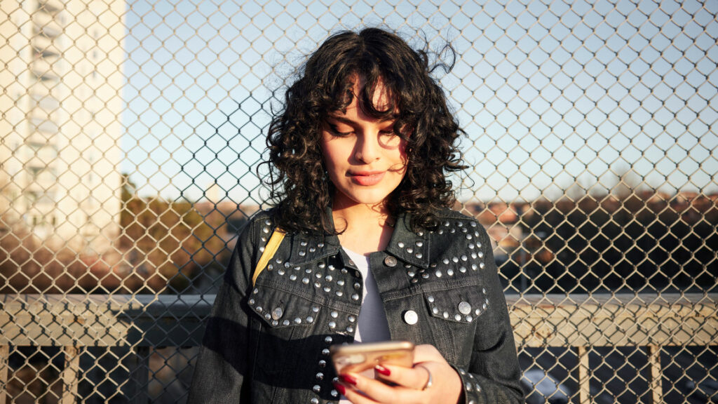 Ung kvinna står ute på en bro och tittar på sin mobiltelefon. 
Johnér Produktion.