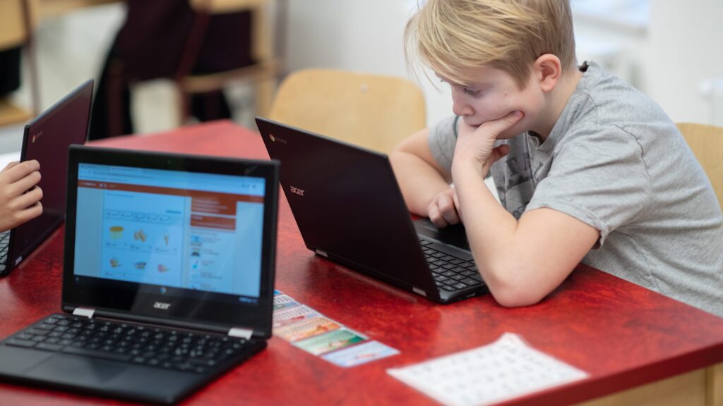 Två unga pojkar sitter vid ett bord i skolan med bärbara datorer.