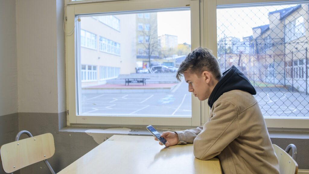 En elev sitter vid ett bord och tittar på sin mobiltelefon