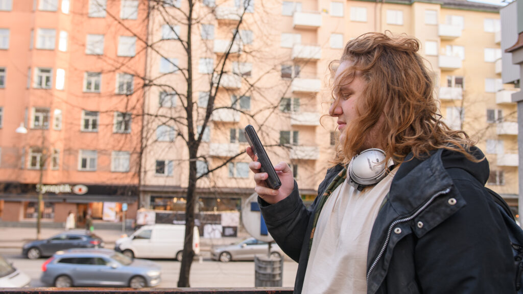 Källkritik på sociala medier. En kvinna går på gatan och tittar på sin mobiltelefon.