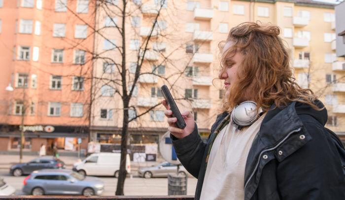 En ung kille står utomhus och scrollar på sin mobil.