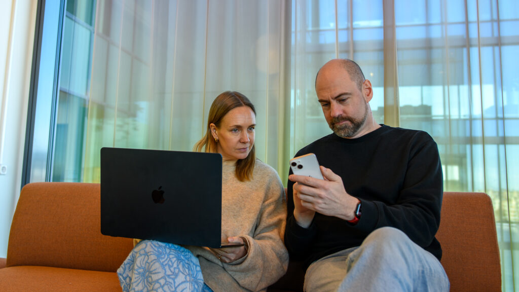 källkritik på sociala medier. Två personer sitter i en soffa, den ena har en laptop i knäet och den andra visar något på sin mobil.