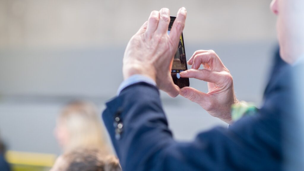 En kostymklädd man som tar en bild med sin mobiltelefon.