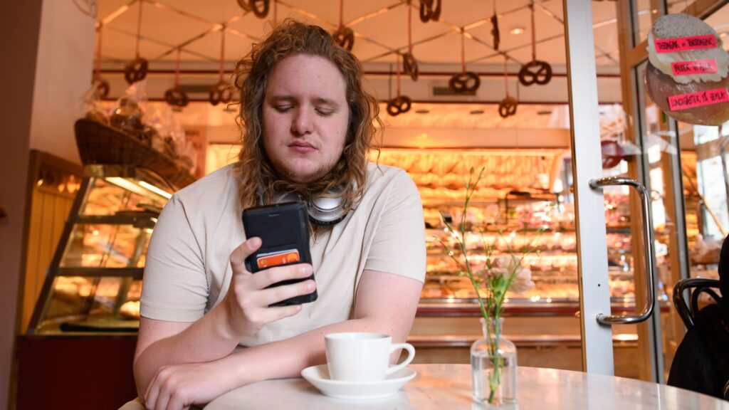 En man sitter vid ett bord och tittar på sin mobiltelefon.