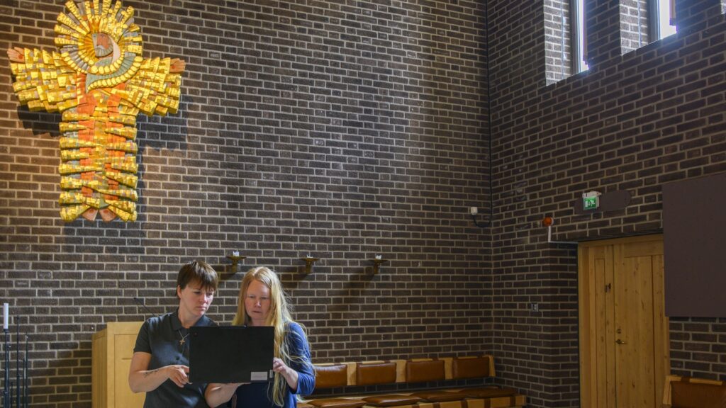 Två kvinnor står i en kyrka och tittar på en dator tillsammans.