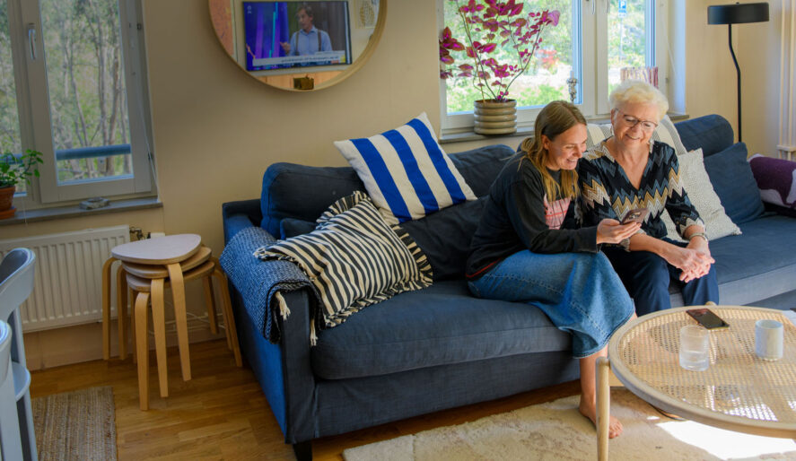 Två kvinnor sitter i en soffa och tittar på en mobil tillsammans.