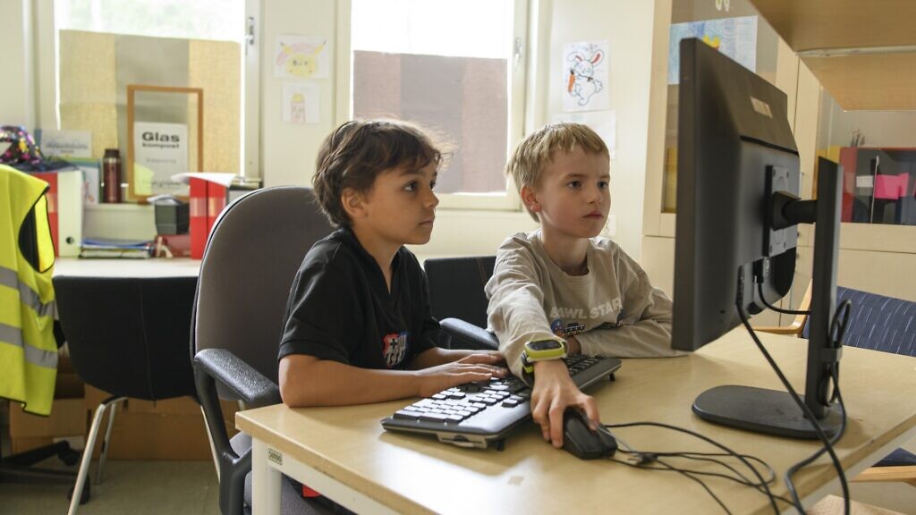 Två barn sitter vid ett skrivbord med en dator.