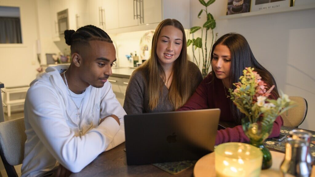 Tre personer sitter vid ett bord och tittar på en bärbar dator.