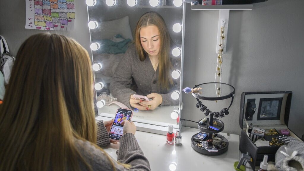 En kvinna sitter framför en spegel och tittar på sin mobiltelefon.