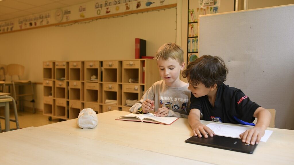 Två barn sitter vid ett bord med en bok.