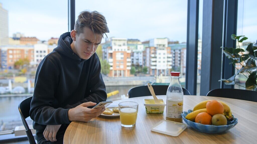 En man sitter vid ett bord och tittar på sin mobiltelefon.