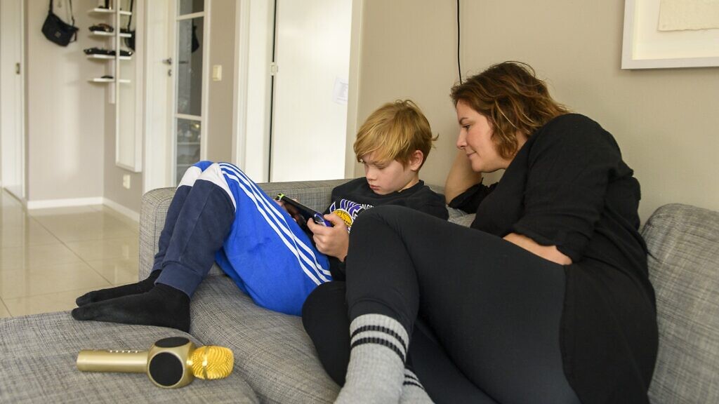 En kvinna och en pojke sitter i en soffa och tittar på en mobiltelefon.