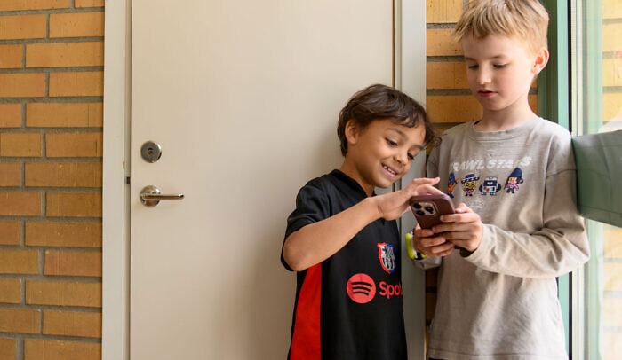 Två barn står tillsammans i en skola och tittar på en mobil.