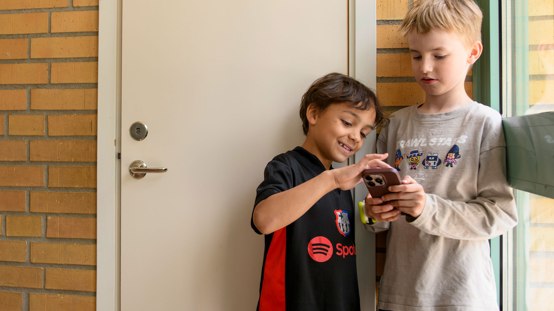 Två barn står tillsammans i en skola och tittar på en mobil.