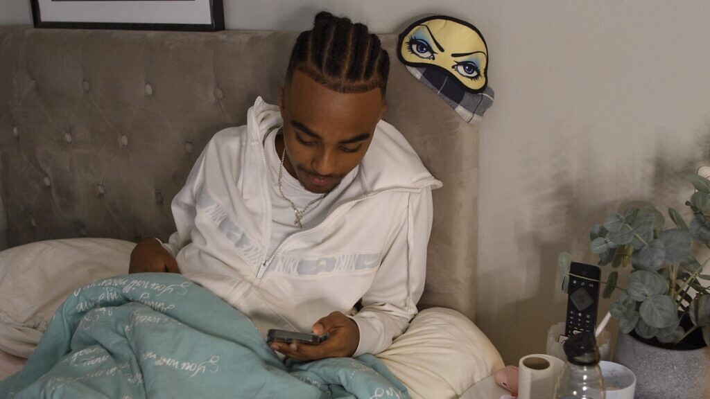 En person som sitter i en säng och tittar på en mobiltelefon.