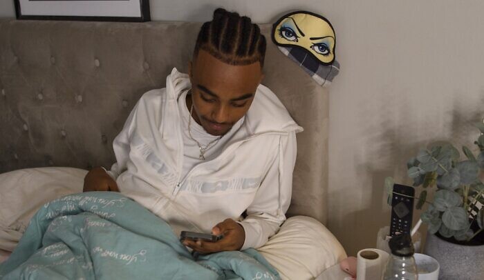 En person som sitter i en säng och tittar på en mobiltelefon.