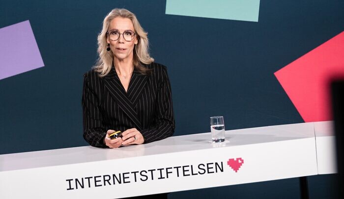 En kvinna med mikrofon presenterar vid ett bord.