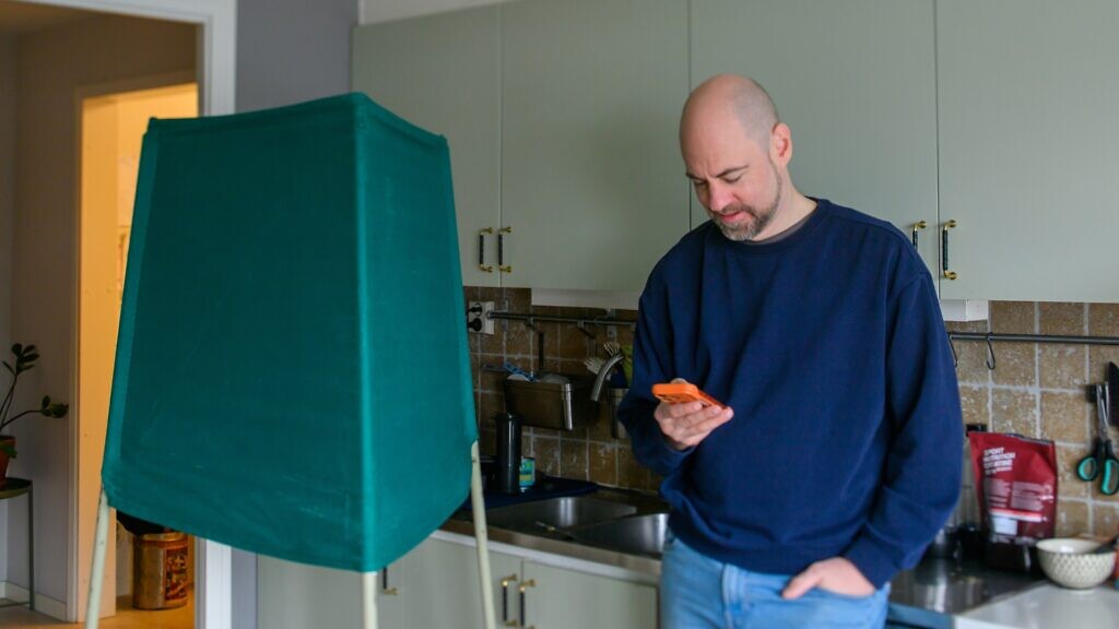 En man står i ett kök och håller i en mobiltelefon.