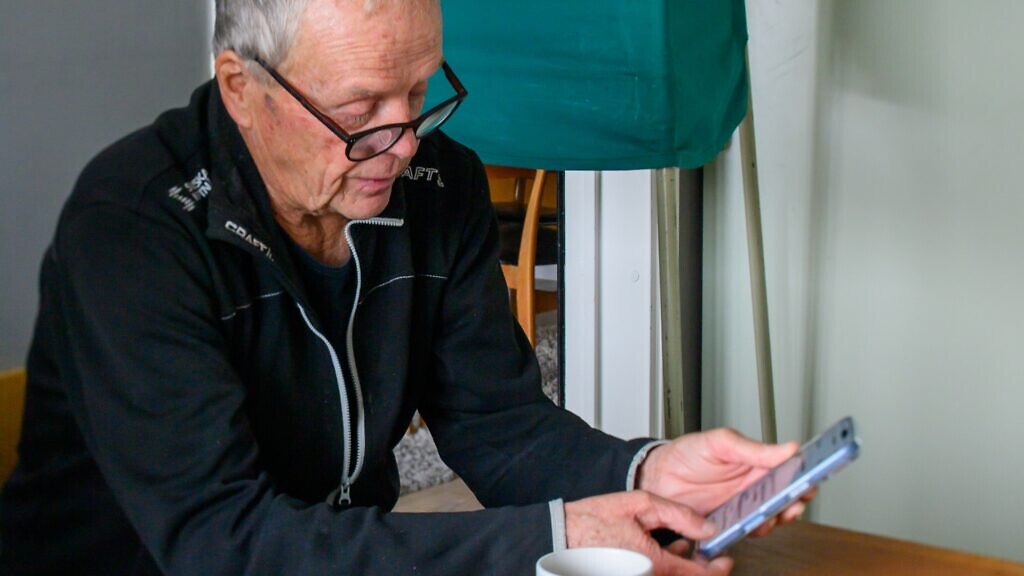 En man sitter vid ett bord och scrollar på mobiltelefon.