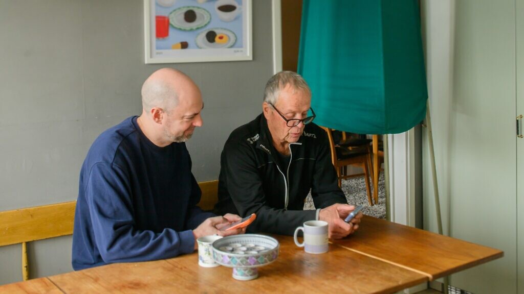 Två män sitter vid ett bord och tittar på en mobiltelefon.