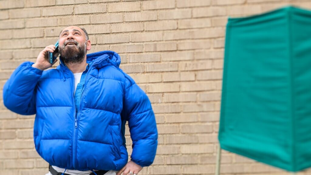 En man står framför en tegelvägg och pratar i mobiltelefon.