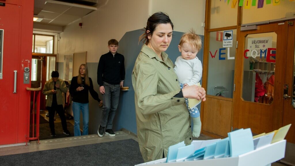 En kvinna med ett spädbarn i famnen tar en valsedel.